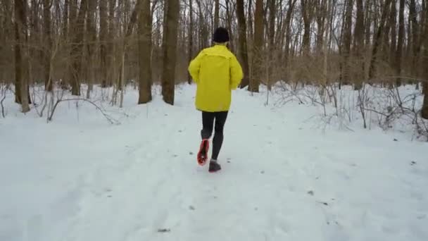 Стеження за зйомками спортивного чоловіка, що бігає в лісі на сніжному покритому шляху в зимовий день — стокове відео