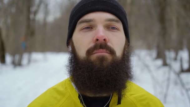 Портрет бородатого человека с голубыми глазами на фоне зимнего леса — стоковое видео