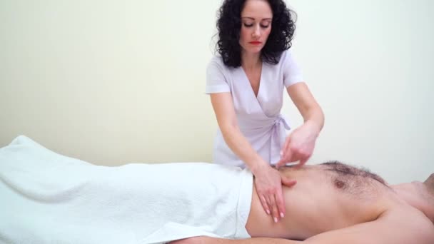 Jovem terapeuta feminino atraente massageando abdômen de cliente masculino no spa — Vídeo de Stock