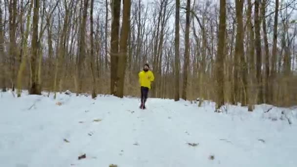 Homme de sport barbu en manteau jaune courant vers la caméra dans la forêt enneigée d'hiver — Video