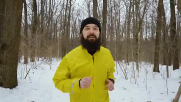Handyaufnahme eines bärtigen Sportlers, der im verschneiten Winterwald auf die Kamera zuläuft — Stockvideo