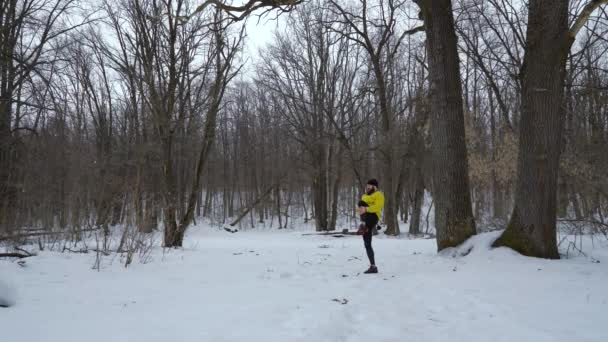 Спортсмен согревается во время снегопада в зимнем лесу с бесплатным пространством — стоковое видео