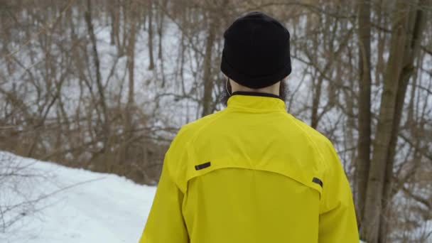 Назад вид спортивного человека начинает бегать вниз по холму в зимнем лесу — стоковое видео