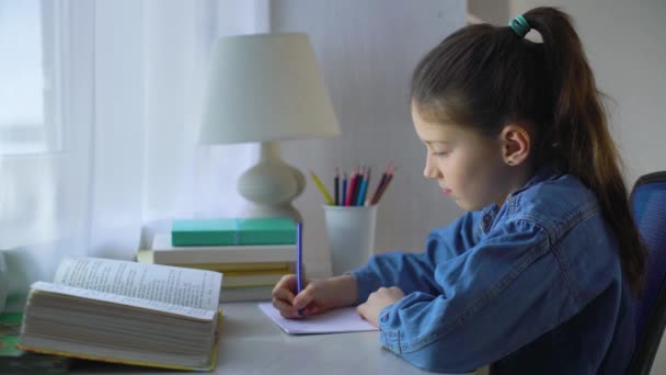 Linda niña de la escuela haciendo la tarea en la mesa — Vídeos de Stock