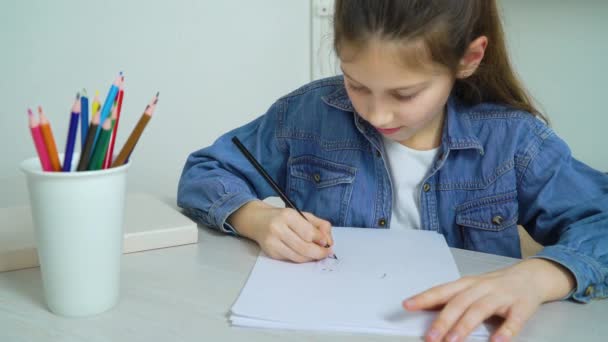Маленька дівчинка в джинсах носить малюнок з кольоровим олівцем вдома — стокове відео
