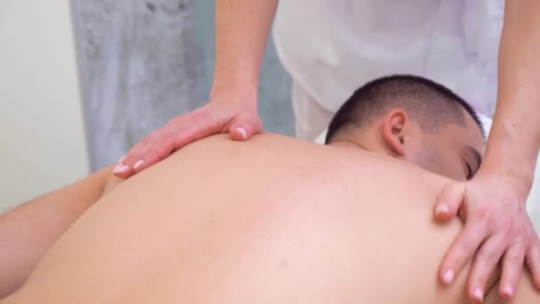 Manos femeninas haciendo masajes relajantes en la parte superior de la espalda del paciente masculino en el salón de spa — Vídeo de stock