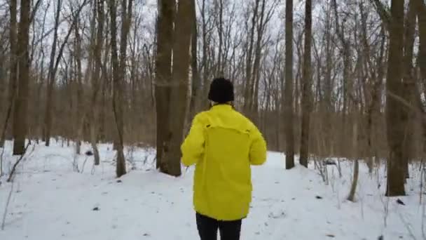 Назад вид спортивного человека, бегущего по снежной тропе в зимнем лесу — стоковое видео