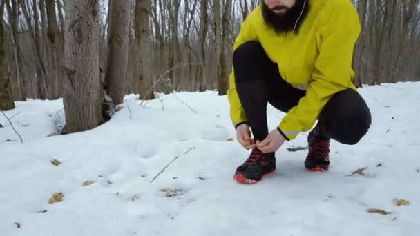 Nízký záběr na muže, který svazuje tkaničky na botce při joggingu v zimním lese — Stock video
