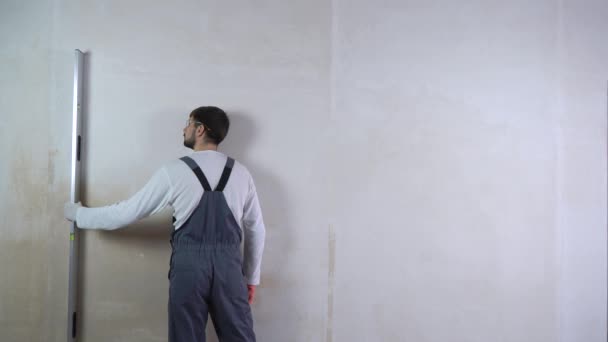 Мужчина строитель проверяет равномерность новой стены с уровнем пузыря с свободным местом — стоковое видео