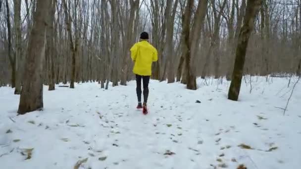 Стеження за зйомками чоловічого спортивного чоловіка, що біжить на снігу в зимовому лісі — стокове відео