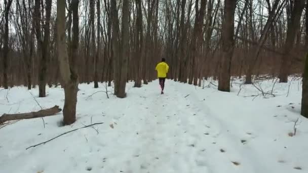 Strzał śledzenia męskiego biegacza w żółtym płaszczu w zimowym lesie — Wideo stockowe