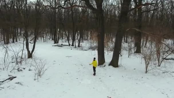 Дуговий постріл спортсмена в жовтому пальто, що пропускає зі стрибковою мотузкою в зимовому лісі — стокове відео