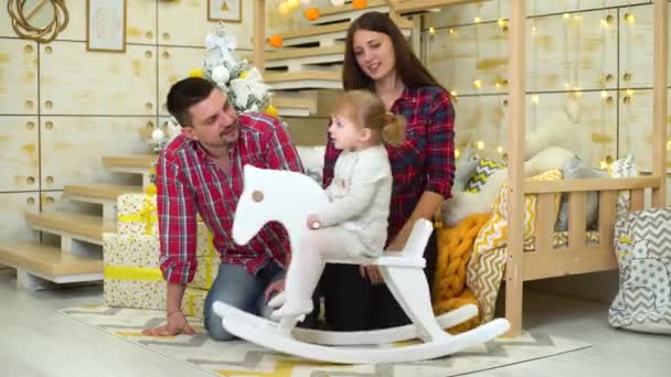 Щаслива сім'я з дочкою малюка на качалковому коні святкує Різдво — стокове відео