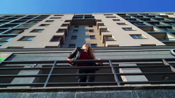 현대 건물의 금속 난간 근처에서 춤추는 금발의 여성의 낮은 각도 샷 — 비디오