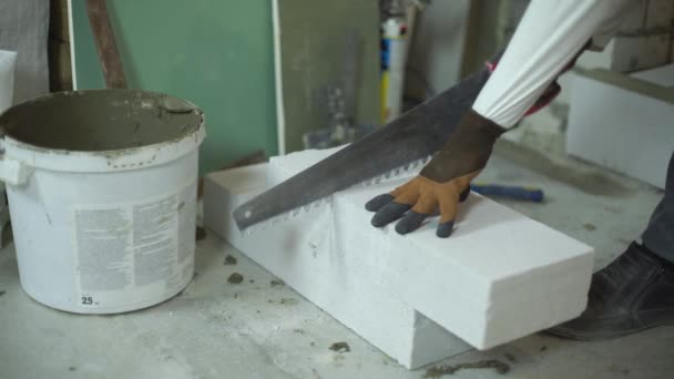 Вид рук строителя, режущих газобетонный блок ручной пилой — стоковое видео