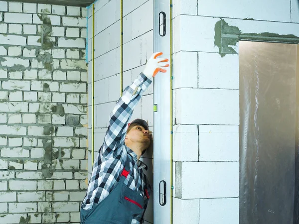 Mann in Arbeit drückt Blasenwaage, um Wand senkrecht zu blockieren — Stockfoto