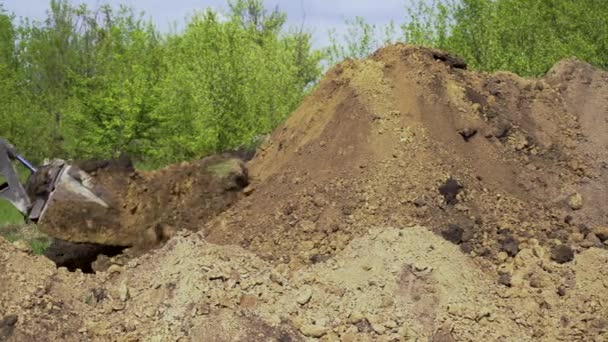 Бульдозер выгружает почву из ведра на земле работает с садом на заднем плане — стоковое видео