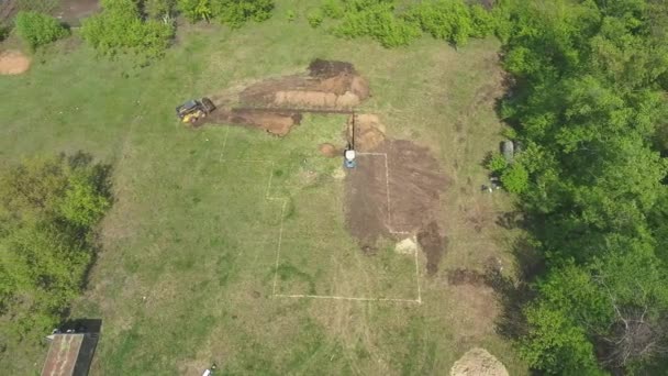 Антенна экскаваторов, копающих почву на зеленом поле с разметкой будущего дома — стоковое видео
