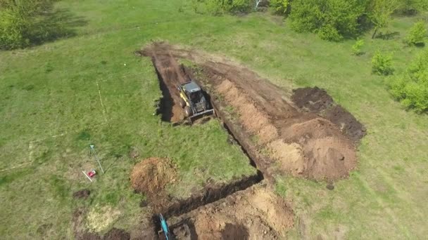 Antena de mini carregador e escavadeira cavando poço fundação no campo gramado — Vídeo de Stock