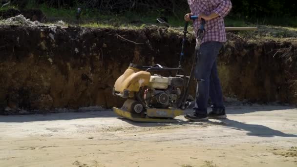Низкий кадр работника с помощью вибрирующего раммера на песчаной поверхности — стоковое видео