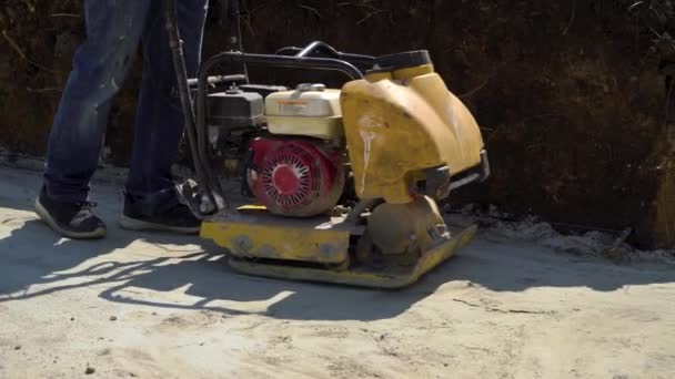 Частичный снимок человека, работающего с вибрирующим пластиновым уплотнителем на поверхности песка — стоковое видео