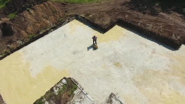 Aérea del hombre que trabaja con el compactador de la placa en el foso de la fundación de la casa nueva — Vídeos de Stock