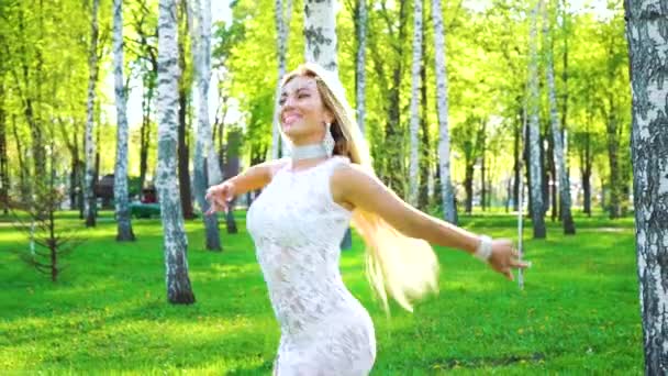 Улыбающаяся женщина в стильном костюме и аксессуарах танцует босиком в березовой роще — стоковое видео