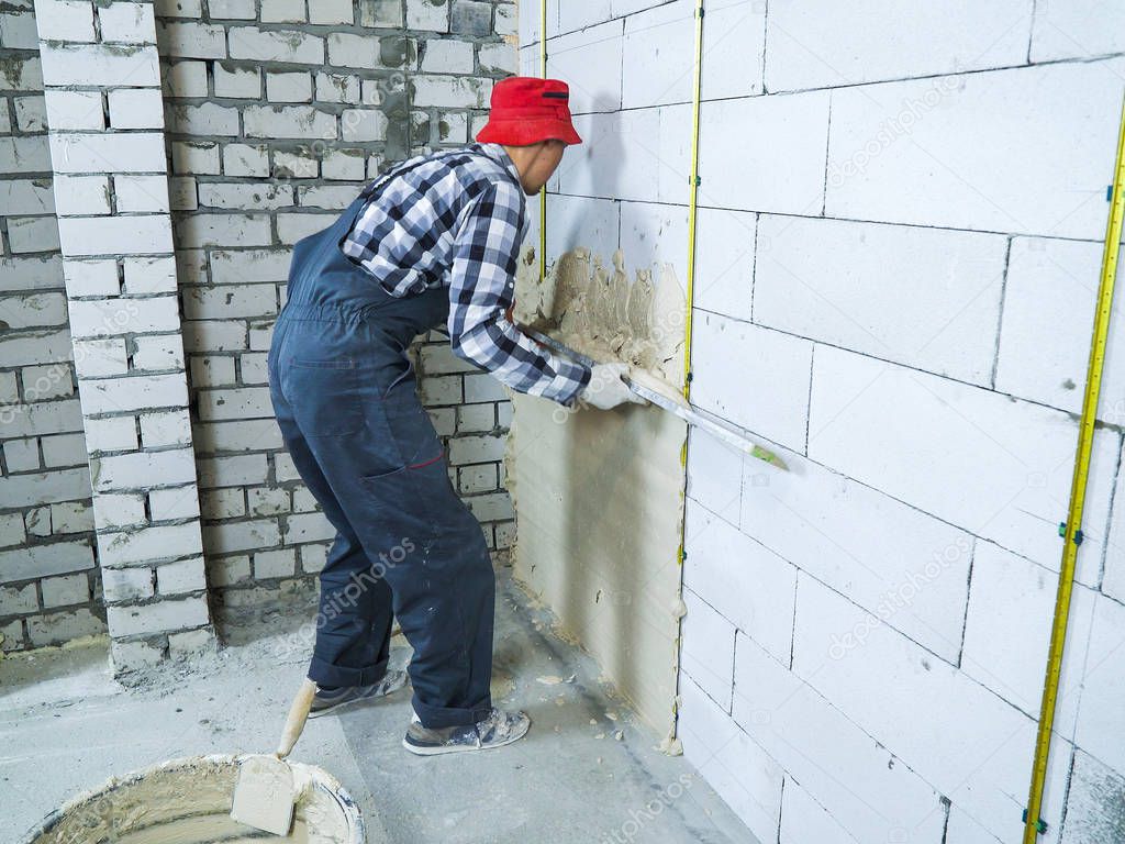 man in work wear spreading plaster on block wall with construction ruler