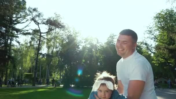 Father swings his little daughter on his arms in summer park with lens flare — Stock Video