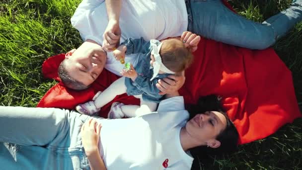 Arriba hacia abajo de los padres con la niña acostada en la manta en el campo de hierba en verano — Vídeo de stock