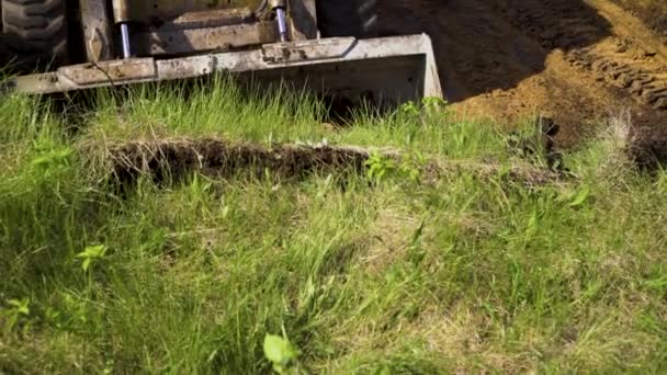 Вид ведра бульдозера, копающего траншею в травянистой почве во время земляных работ — стоковое видео