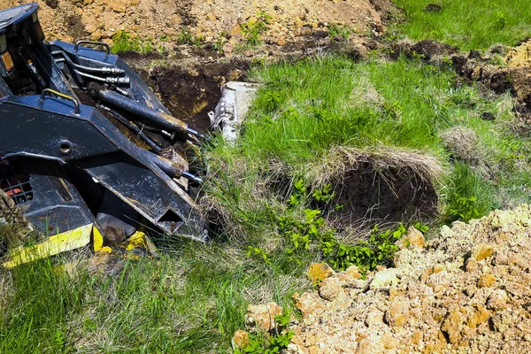 Обрезанный вид выкапывания ямы мини-погрузчика во время земляных работ на травянистом поле — стоковое фото