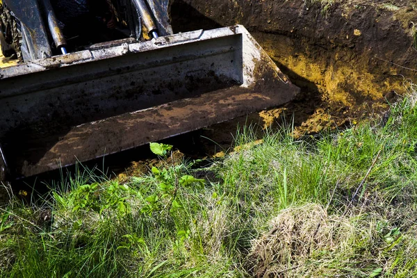 Lerig grävskopa hink kommer att gräva jorden i gräsmark i landskapet — Stockfoto