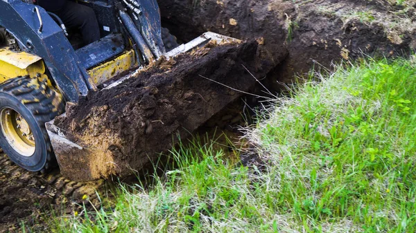Vista ritagliata di secchio di escavatore con terreno in esso a lavori di terra su campo erboso — Foto Stock