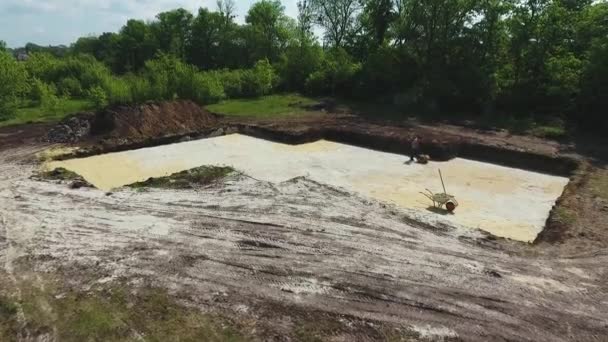 Aerial of man ramming sand with vibratory plate compactor in foundation pit — Stock Video