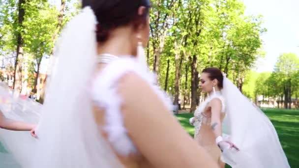 Красивый жених смотрит на красивых невест, гуляющих вокруг него в солнечном парке — стоковое видео