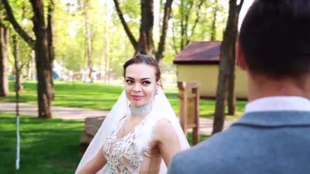美しい若い花嫁はまだ日当たりの良い公園に立って新郎の周りを歩く — ストック動画