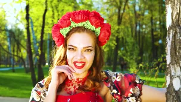 Attractive young woman in folklore costume and flower circlet smiling at camera — Stock Video