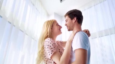 Pijamalı genç adam ve kadından uzaklaş. Perdeli pencerenin yanında sarılıyorlar.