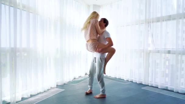 Hombre joven sostiene a la mujer en sus brazos y gira en una habitación espaciosa — Vídeos de Stock