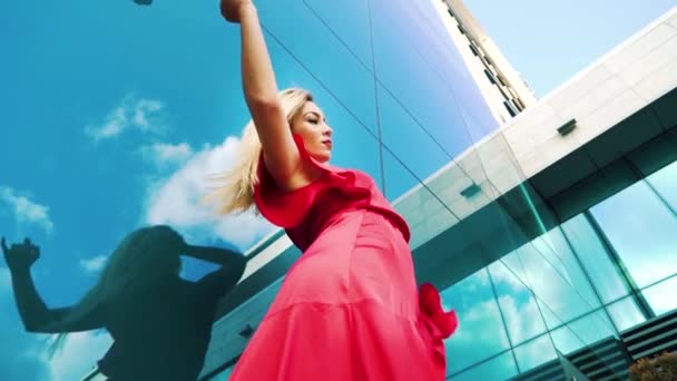 Tiro de ángulo bajo de mujer rubia en vestido rojo bailando cerca de edificio moderno — Vídeos de Stock