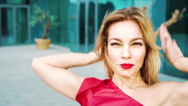 Porträt einer hübschen blonden Frau mit rotem Lippenstift im roten Kleid, die draußen tanzt — Stockvideo