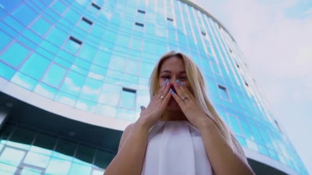 Lage hoek van jonge blonde vrouw lachen om camera met wolkenkrabber op achtergrond — Stockvideo