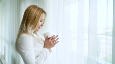 pencereden dışarı bakarak ve kahve içme güzel sarışın kadın yan görünümü