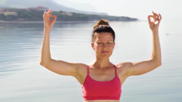 Tiro de arco de mujer practicando yoga manteniendo los dedos en gesto mudra a orillas del mar — Vídeo de stock