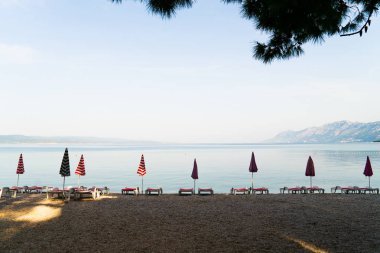arka planda deniz ve dağlar ile boş plajda güneş şemsiye ve şezlong