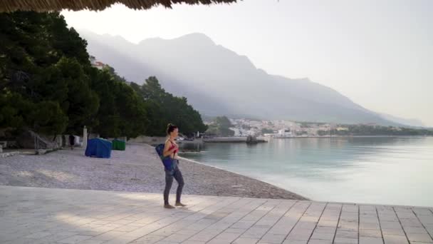 Barefoot vrouw in Sportswear met yoga mat wandelingen op steen bestrating aan zee — Stockvideo