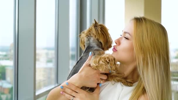 Portrait of beautiful blonde woman holding small fluffy dog kissing her — Stock Video