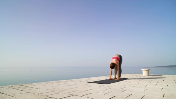 Sportos nő csinál jóga kő Boardwalk a tenger és az ég a háttérben — Stock videók