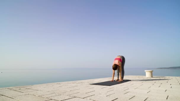 Mujer atlética haciendo yoga en el paseo marítimo de piedra con mar y cielo en el fondo — Vídeo de stock